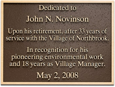 Bronze cast plaque with dedication text, mounted on a light wood board.