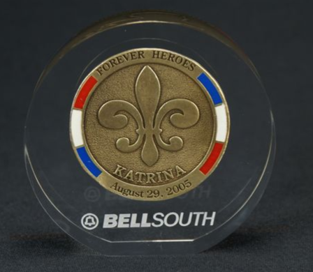 Clear acrylic circle embedment with a bronze "Forever Heroes Katrina" coin featuring a fleur-de-lis and red, white, blue trim.