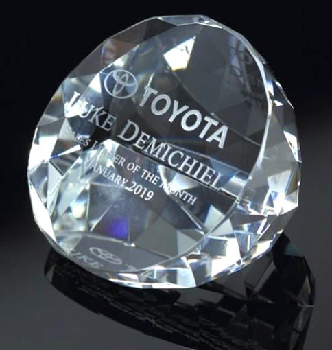 Clear optic crystal round paperweight, faceted with engraved Toyota logo and "Luke Demichiel" text.