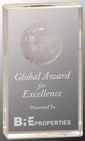 Clear crystal block award with etched Earth dome, "Global Award for Excellence," and "B&E PROPERTIES" logo.