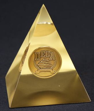 Shiny gold pyramid award with a circular DECA logo embedded on one side.