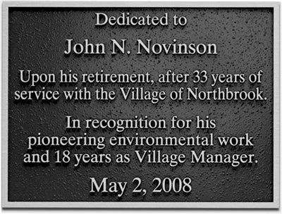 Dark bronze cast plaque with raised text for John N. Novinson, commemorating retirement and environmental work.