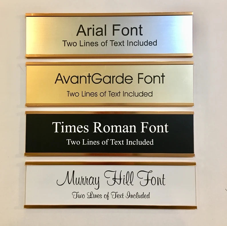 Four wall nameplates with gold holders, showing Arial (silver), AvantGarde (gold), Times Roman (black), and Murray Hill (white) fonts.