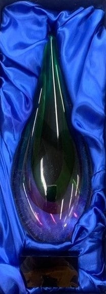 Clear tear drop glass art with colorful peacock tail design on a dark base, nestled in blue satin.